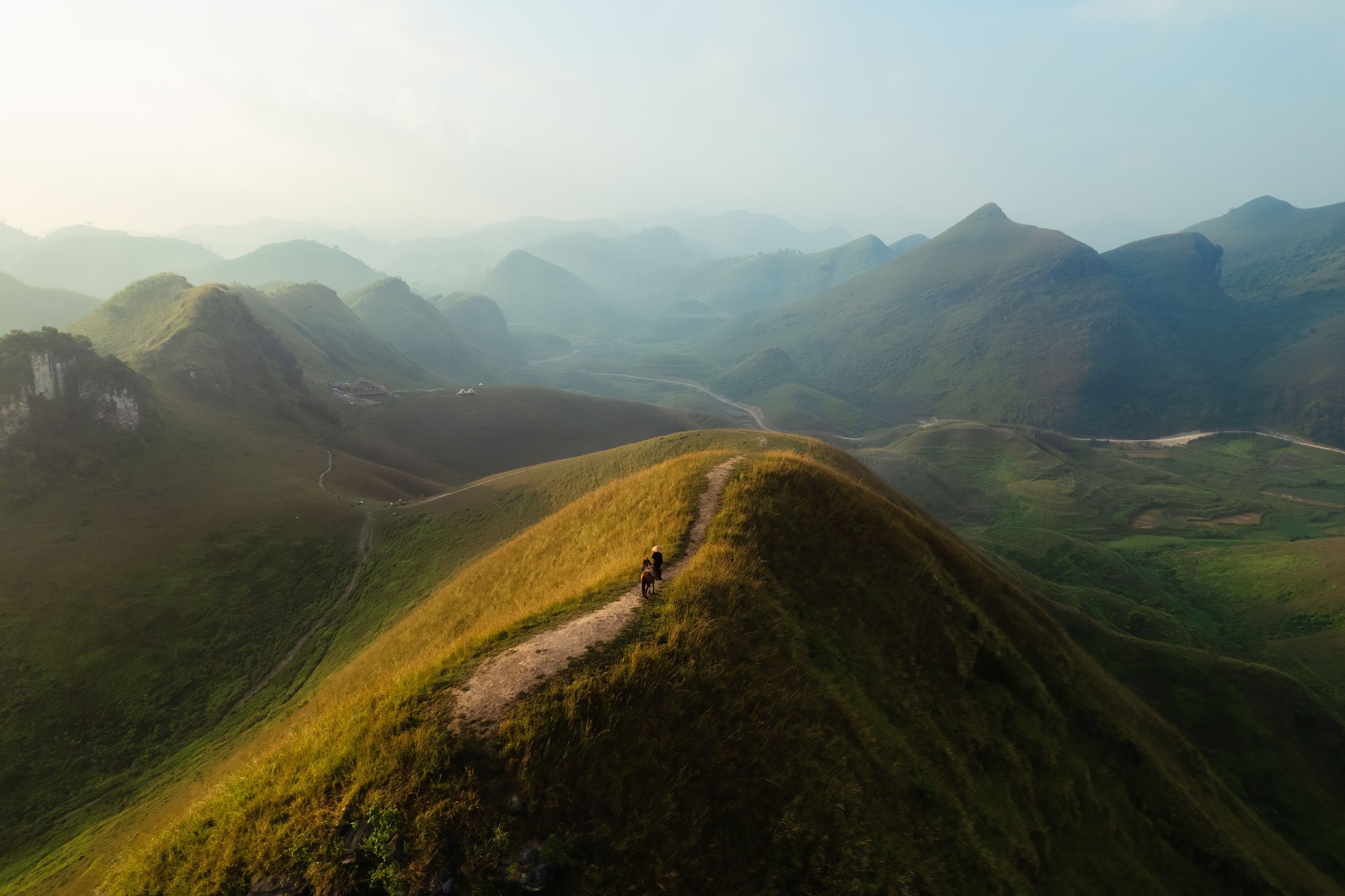 Aerial view of Ba Guang grass hill, Mountain range with fog and villager bringing horse to graze on the mountain in the morning